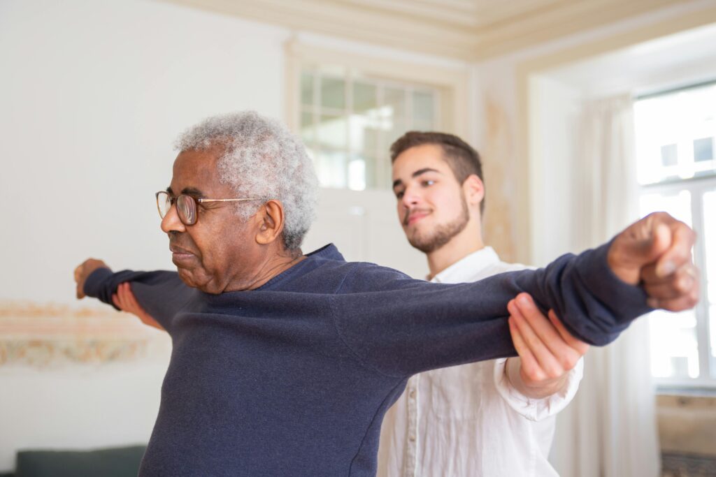 Is a Pilot Immigration Program the Best Option for You? A senior man is assisted by a caregiver for stretching exercises indoors.